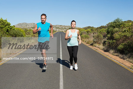 Fit couple jogging on the open road together on a sunny day