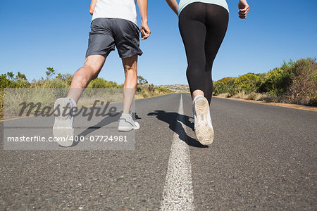 Fit couple running on the open road together on a sunny day