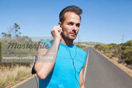 Athletic man adjusting his earphones on a run on a sunny day