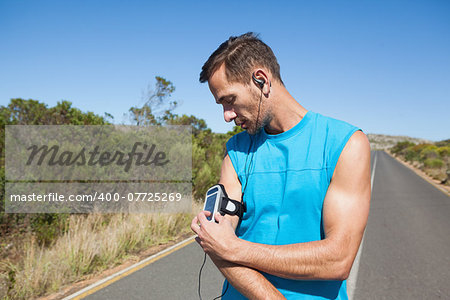 Athletic man adjusting his music player on a run on a sunny day