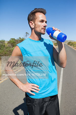 Athletic man on open road taking a drink on a sunny day