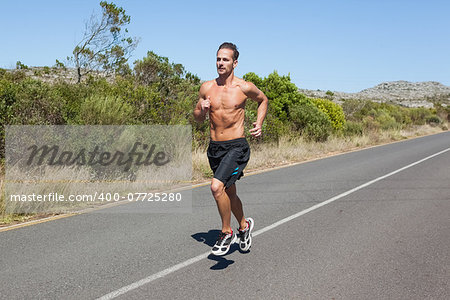 Shirtless man jogging on open road  on a sunny day