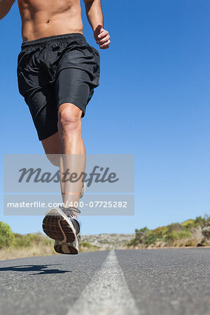 Shirtless man jogging on open road on a sunny day