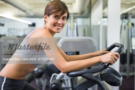 Fit brunette working out on the exercise bike at the gym