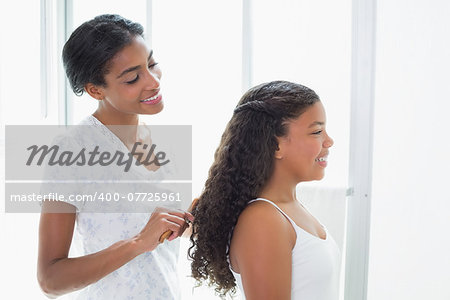 Pretty mother brushing her daughters hair at home in bathroom