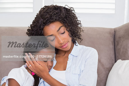 Pretty mother sitting on the couch with her sleeping daughter  at home in the living room