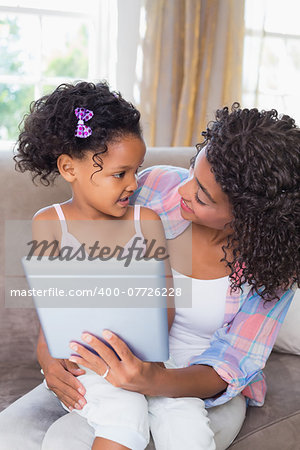 Pretty mother sitting on couch with cute daughter using tablet together at home in the living room