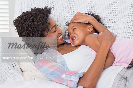 Cute daughter lying with mother on the sofa at home in the living room