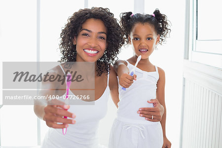 Pretty mother and daughter showing toothbrushes at home in the bathroom