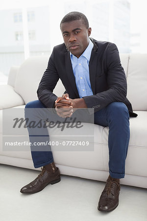 Serious businessman looking at camera on couch at home in the living room