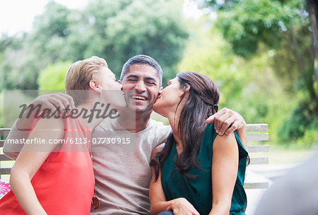 Women kissing man's cheeks outdoors