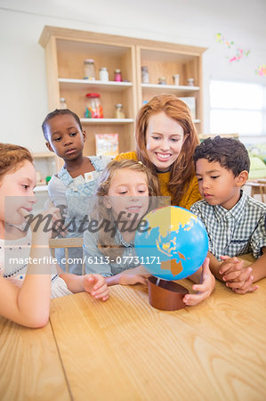 Students and teacher examining globe in classroom