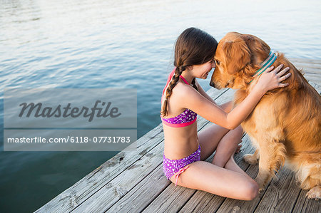 A young girl and a golden retriever dog sitting on a jetty.