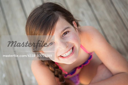 A young girl seated on a jetty looking upwards.