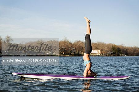 A woman doing a headstand on a paddle board on lake