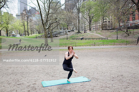 A young woman in Central Park, in a black leotard and leggings, doing yoga.