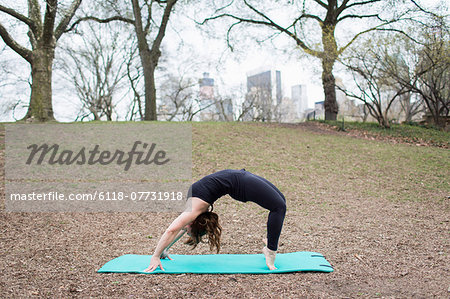 A young woman in Central Park, in a black leotard and leggings, doing yoga.