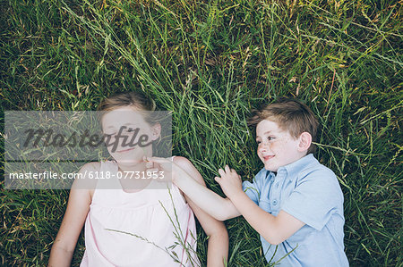 Two children, brother and sister lying side by side on the grass