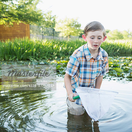 A young boy standing thigh deep in water, with a fishing net.