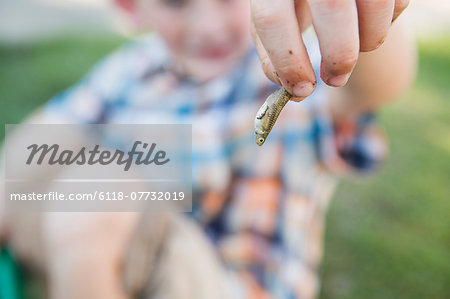 A young boy holding a small fish in his fingers.