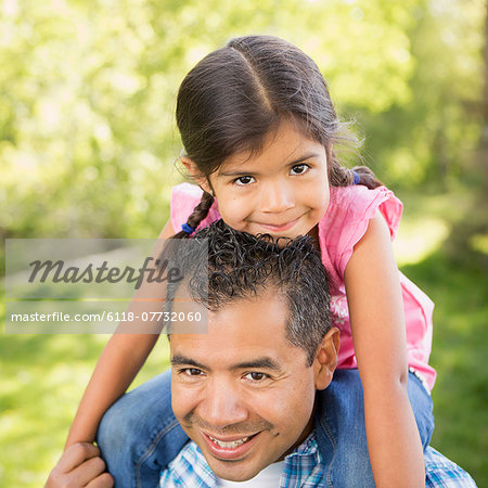 A man giving his daughter a piggyback ride on his shoulders.