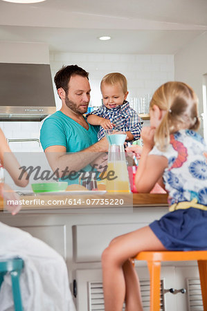 Father multi tasking breakfast with son and daughters