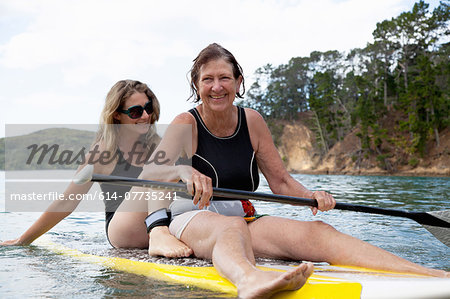 Senior woman and daughter paddleboarding at sea