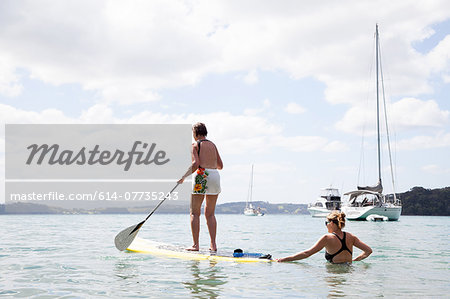 Daughter pushing senior mothers paddleboard at sea