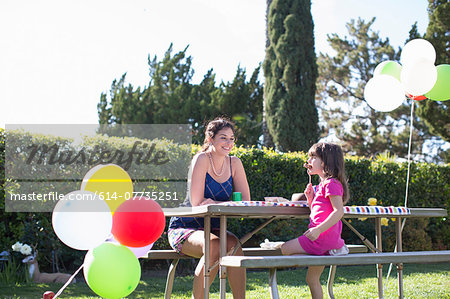 Mother and daughter sitting at party table in garden