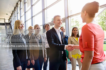 Team of business men and women greeting client in office