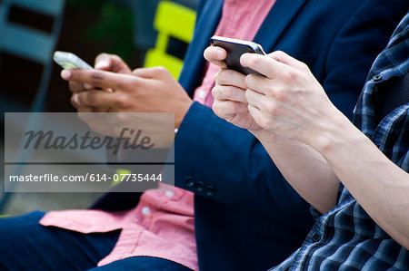 Cropped torso shot of young businessmen in city park texting on smartphones