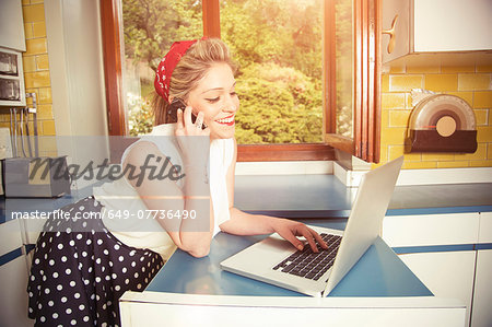 Young woman wearing vintage clothes using laptop and cellphone