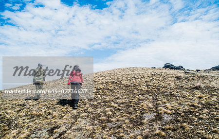 Rear view of two young women hiking up mountain