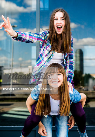 Two young women making peace signs and piggybacking