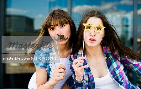 Portrait of two young women holding up mustache and specs costume masks