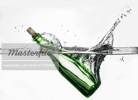 Surface level view of green bottle splashing into clear water