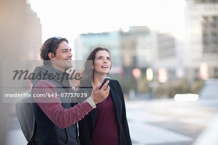 Couple with smartphone looking up on city street