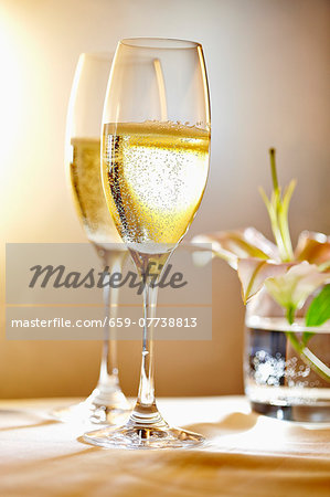 Two glasses of champagne in front of a vase of flowers