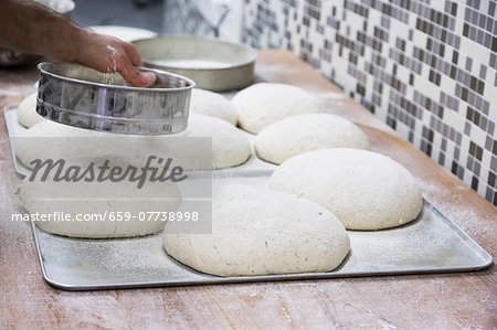 Hands sprinkling flour on loaves of unbaked bread