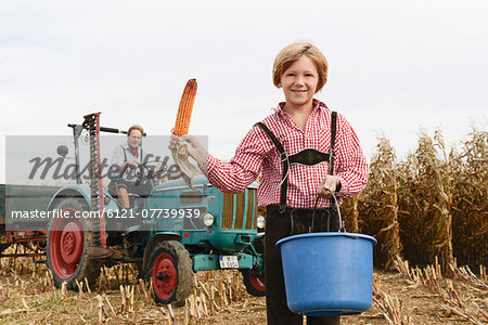 Father and son on tractor in cornfield, Bavaria, Germany