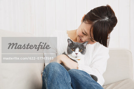 Japanese young woman in jeans and white shirt with cat on the sofa