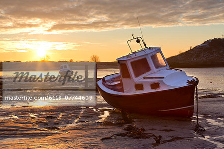 View towards the Aln Estuary during a stunning winter sunrise from the beach at low tide with a fishing boat in the foreground, Alnmouth, near Alnwick, Northumberland, England, United Kingdom, Europe