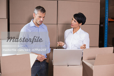 Pretty warehouse manager using laptop with colleague in a large warehouse