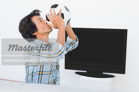 Side view of a football fan kissing ball against tv