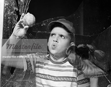 1950s BOY IN TEE-SHIRT & CAP REMOVING BASEBALL FROM BROKEN WINDOW