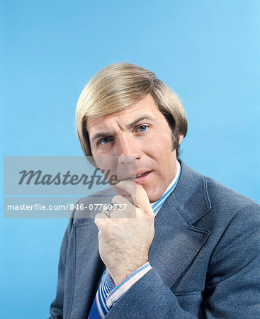 1960s 1970s PORTRAIT OF BUSINESSMAN IN SUIT AND TIE WITH QUIZZICAL EXPRESSION LOOKING AT CAMERA HAND NEAR MOUTH
