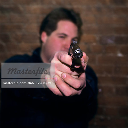 1990s YOUNG MAN LOOKING AT CAMERA AND POINTING GUN