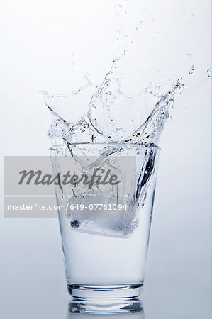 Ice cube splashing into glass of clear water