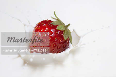 Fresh strawberry splashing onto milk surface