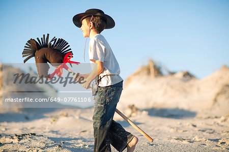 Boy with hobby horse dressed as cowboy in sand dunes